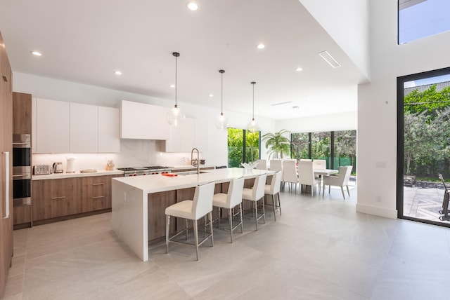 kitchen with a kitchen island with sink, white cabinetry, tasteful backsplash, sink, and a breakfast bar