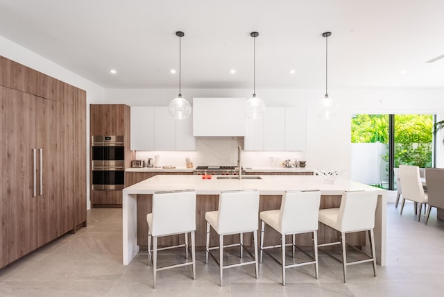 kitchen with a breakfast bar area, white cabinets, a kitchen island with sink, sink, and double oven