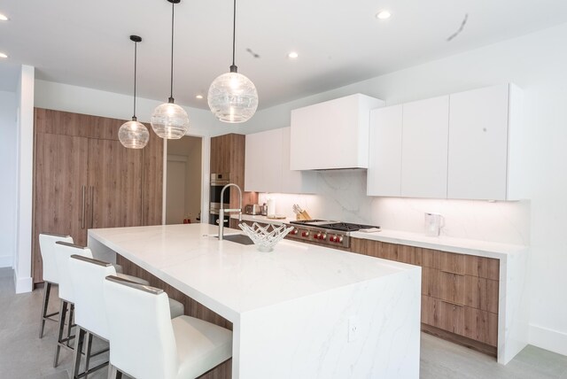 kitchen with white cabinets, stainless steel gas stovetop, pendant lighting, decorative backsplash, and a kitchen island with sink