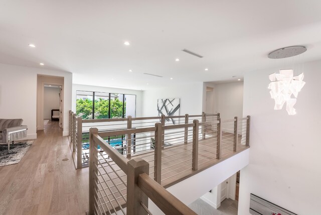 hall featuring light wood-type flooring, baseboard heating, and an inviting chandelier