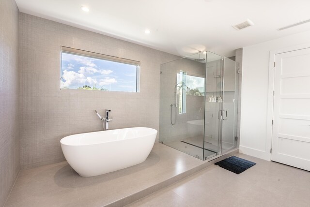 bathroom featuring plus walk in shower and tile walls