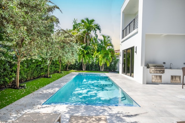 view of pool with area for grilling, sink, and a patio