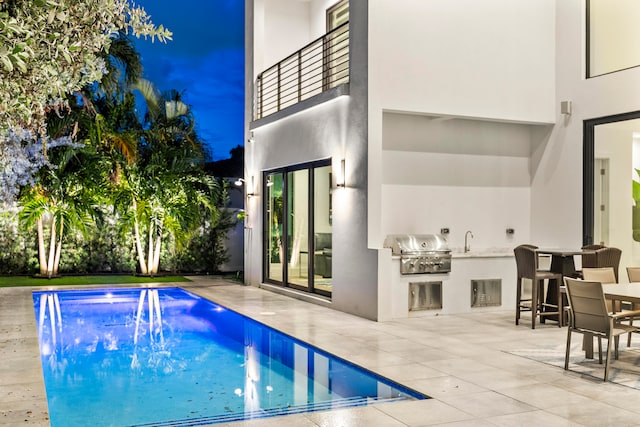 pool at night with a grill, an outdoor kitchen, and a patio