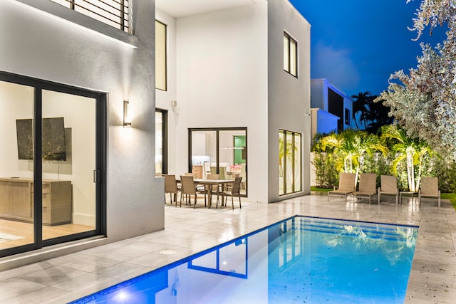 pool at night featuring a patio area