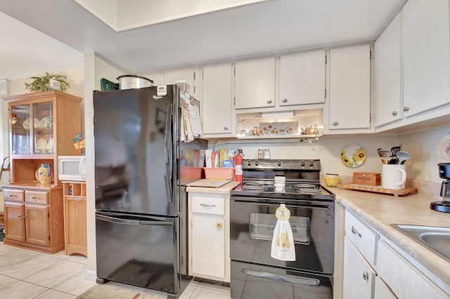 kitchen with black appliances, light tile patterned floors, sink, and white cabinetry