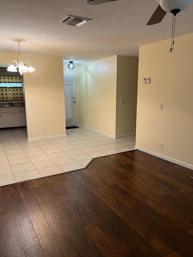 spare room featuring light wood-type flooring, a textured ceiling, and ceiling fan with notable chandelier