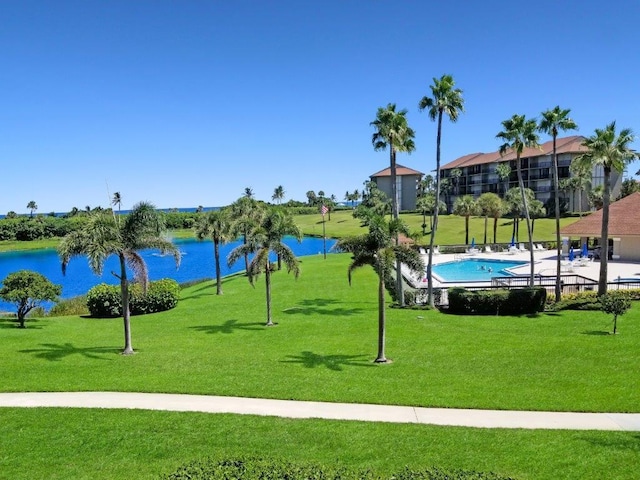 surrounding community with a pool, a water view, and a yard