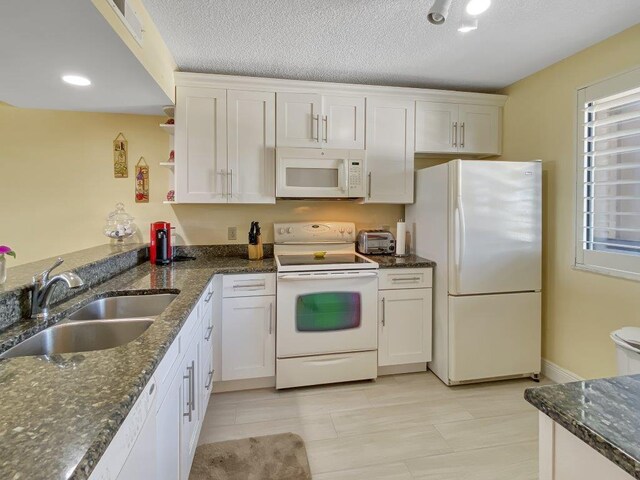 kitchen featuring white cabinetry, sink, white appliances, and dark stone counters