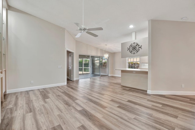 unfurnished living room featuring high vaulted ceiling, ceiling fan with notable chandelier, and light wood-type flooring