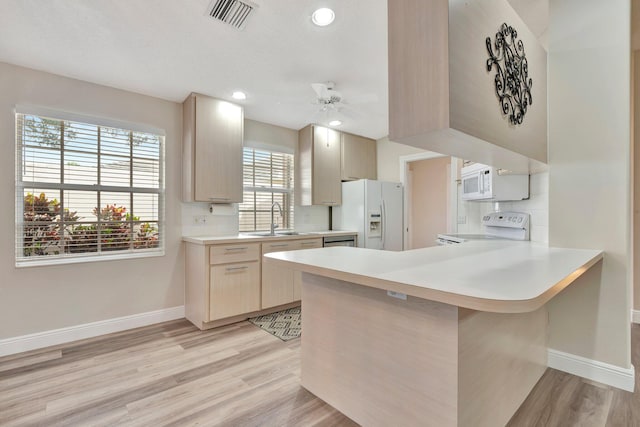 kitchen with kitchen peninsula, white appliances, sink, light brown cabinets, and light hardwood / wood-style floors