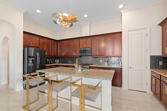 kitchen featuring light stone counters, stainless steel appliances, a kitchen island with sink, sink, and decorative light fixtures