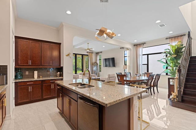 kitchen featuring dishwasher, a kitchen island with sink, sink, ceiling fan, and light stone counters