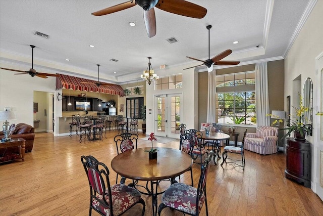 dining space with ceiling fan with notable chandelier, light wood-type flooring, french doors, and a raised ceiling