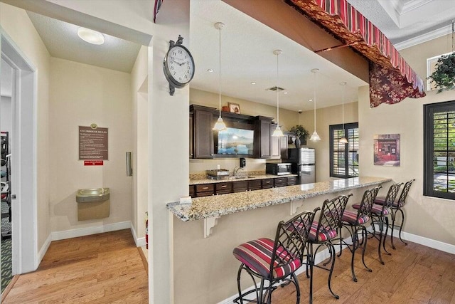 kitchen with pendant lighting, a breakfast bar area, light stone countertops, light hardwood / wood-style flooring, and kitchen peninsula