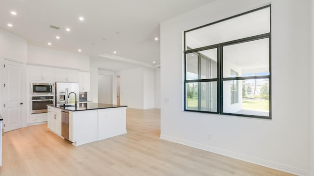 kitchen featuring appliances with stainless steel finishes, a kitchen island with sink, white cabinetry, and light hardwood / wood-style floors