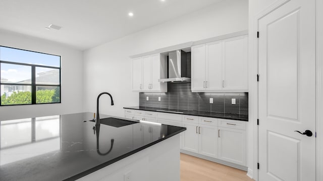 kitchen featuring wall chimney range hood, tasteful backsplash, white cabinetry, light hardwood / wood-style floors, and sink