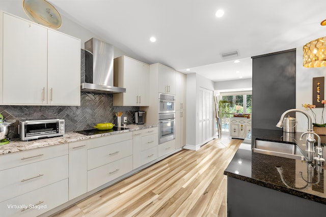 kitchen with stone counters, white cabinetry, sink, black electric stovetop, and wall chimney exhaust hood