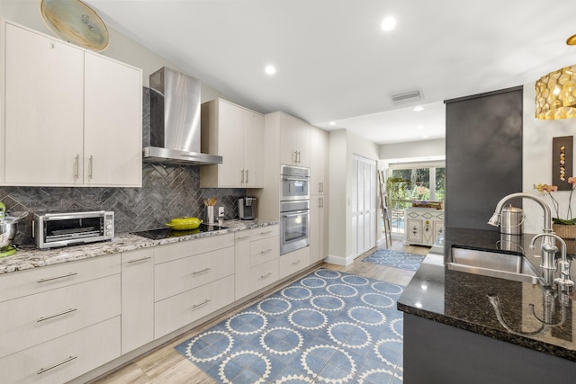 kitchen with stone countertops, sink, white cabinets, wall chimney range hood, and black electric cooktop