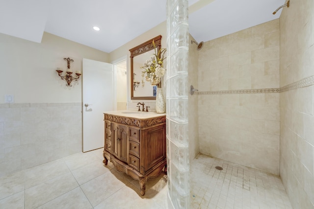 bathroom featuring vanity, a tile shower, tile patterned flooring, and tile walls