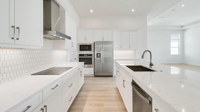 kitchen with light stone countertops, sink, wall chimney range hood, appliances with stainless steel finishes, and light wood-type flooring