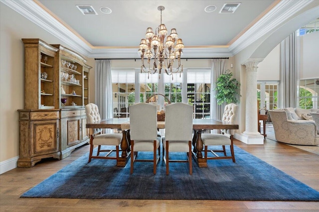 dining room featuring decorative columns, crown molding, wood-type flooring, and a notable chandelier