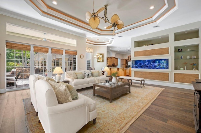 living room with a tray ceiling, dark hardwood / wood-style flooring, and built in features