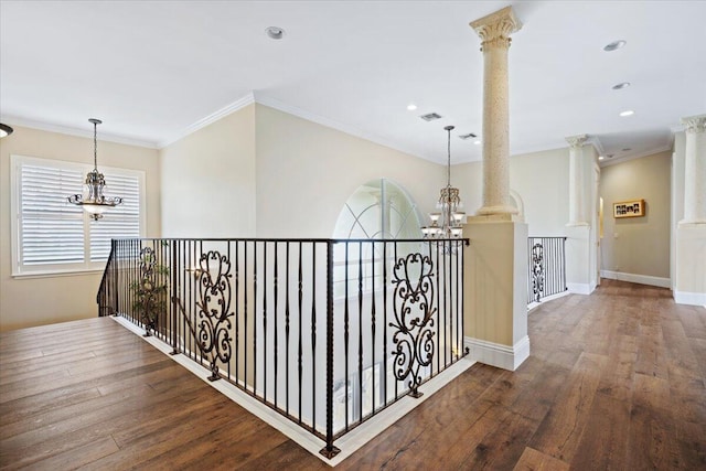 hall with decorative columns, crown molding, hardwood / wood-style flooring, and an inviting chandelier