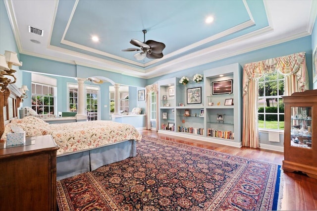 bedroom with ornate columns, ornamental molding, a tray ceiling, ceiling fan, and wood-type flooring