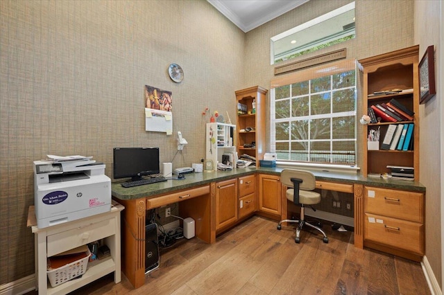 home office featuring crown molding, built in desk, and light wood-type flooring