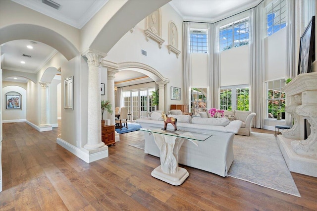 living room featuring hardwood / wood-style floors, ornate columns, crown molding, and a high ceiling