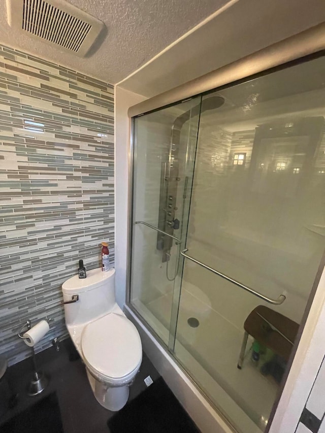 bathroom with decorative backsplash, toilet, a shower with door, and a textured ceiling