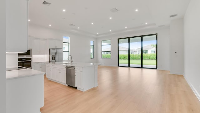 kitchen with light wood-type flooring, stainless steel appliances, sink, a center island with sink, and white cabinetry