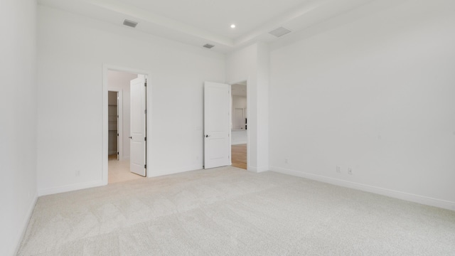 unfurnished bedroom featuring light colored carpet, a spacious closet, a tray ceiling, and ensuite bath