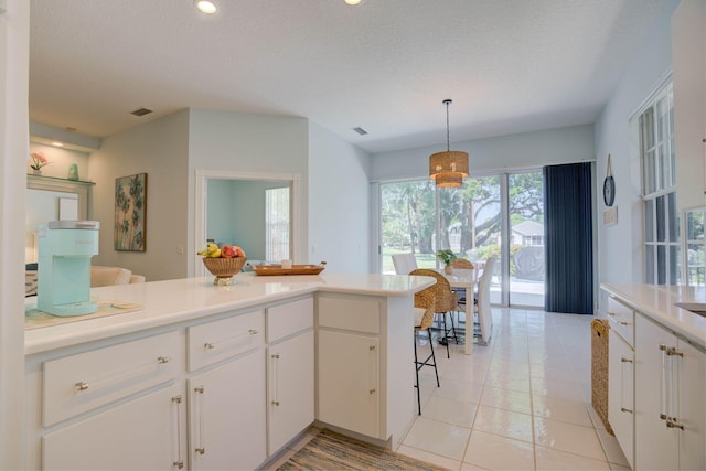 kitchen with a breakfast bar area, white cabinetry, pendant lighting, and a textured ceiling