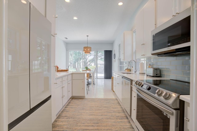 kitchen featuring white cabinetry, sink, stainless steel appliances, tasteful backsplash, and decorative light fixtures