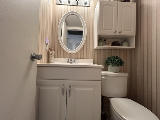 bathroom with vanity, wood walls, and toilet