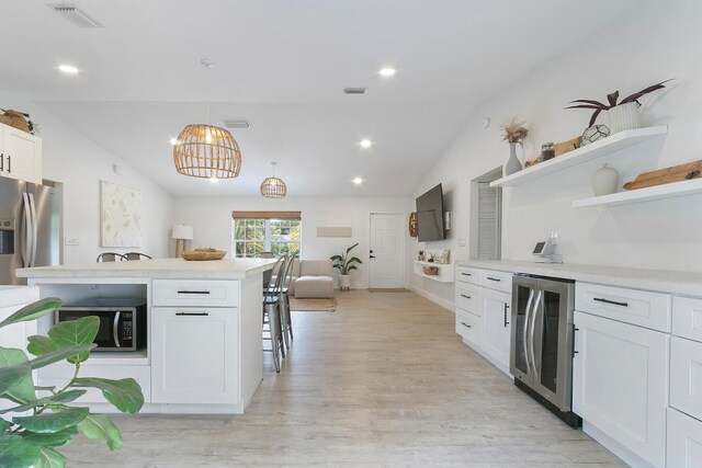 kitchen featuring stainless steel appliances, light wood-type flooring, lofted ceiling, white cabinetry, and beverage cooler