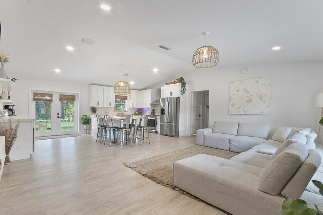 living room with an inviting chandelier, lofted ceiling, french doors, and light wood-type flooring