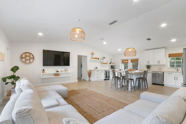 living room with a healthy amount of sunlight, vaulted ceiling, light hardwood / wood-style flooring, and an inviting chandelier