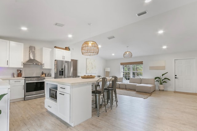 kitchen featuring tasteful backsplash, stainless steel appliances, wall chimney range hood, light hardwood / wood-style floors, and a center island