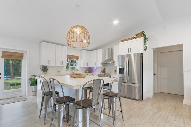 kitchen with decorative backsplash, wall chimney exhaust hood, vaulted ceiling, appliances with stainless steel finishes, and light hardwood / wood-style flooring