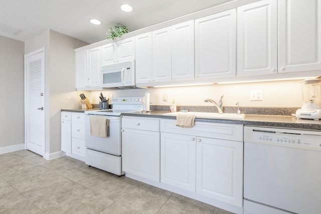 kitchen featuring dark countertops, white appliances, white cabinetry, and a sink