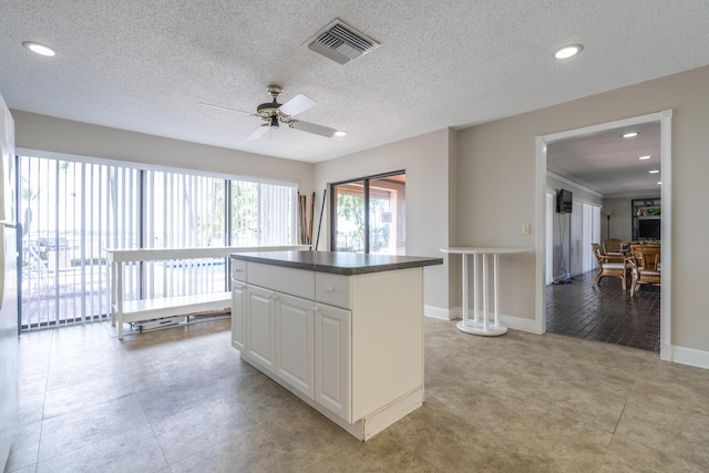 kitchen with baseboards, visible vents, white cabinets, dark countertops, and a kitchen island