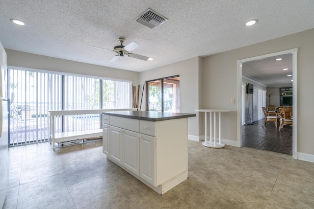 kitchen with visible vents, baseboards, dark countertops, a center island, and white cabinetry