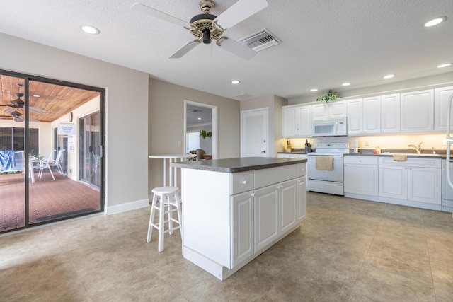 kitchen with dark countertops, white appliances, white cabinets, and a center island