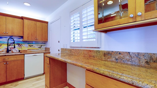 kitchen with light stone counters, brown cabinets, glass insert cabinets, white dishwasher, and a sink