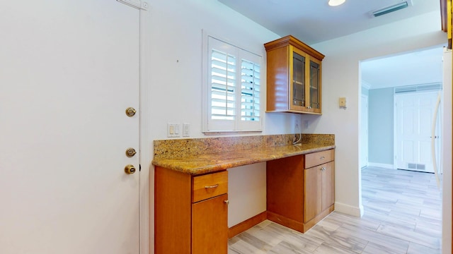 kitchen featuring glass insert cabinets, light stone countertops, visible vents, and brown cabinets