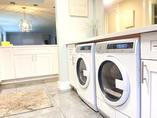 clothes washing area featuring washing machine and clothes dryer, cabinets, and an inviting chandelier