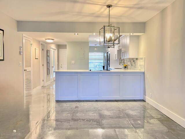 kitchen with a peninsula, a chandelier, light countertops, baseboards, and pendant lighting