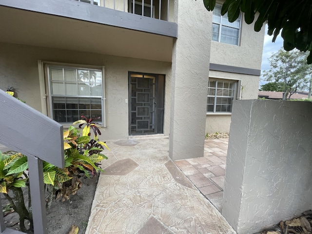 doorway to property with stucco siding, a patio, and fence